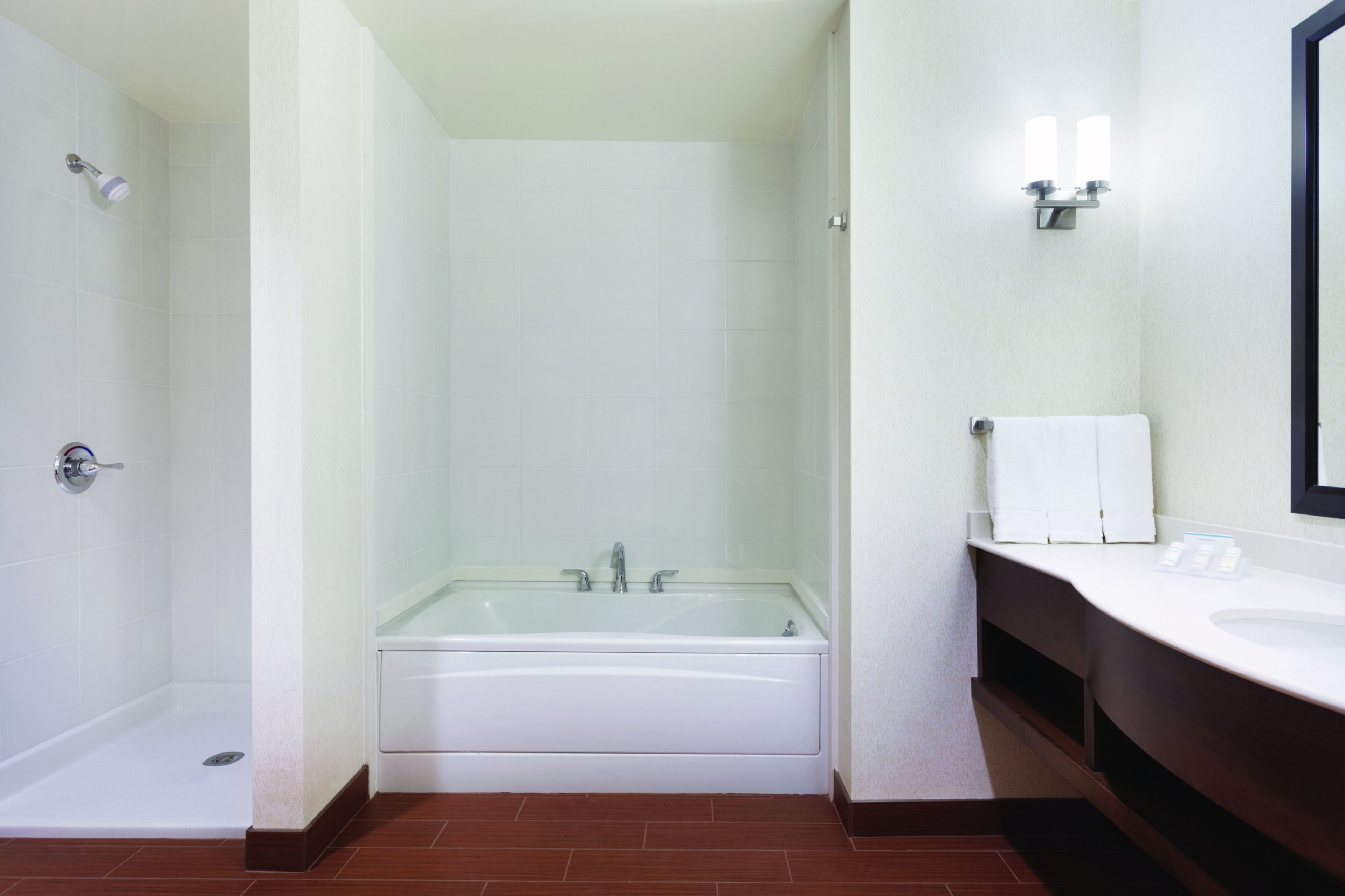 A modern bathroom with a glass-enclosed shower, a white bathtub, and a vanity with a mirror.