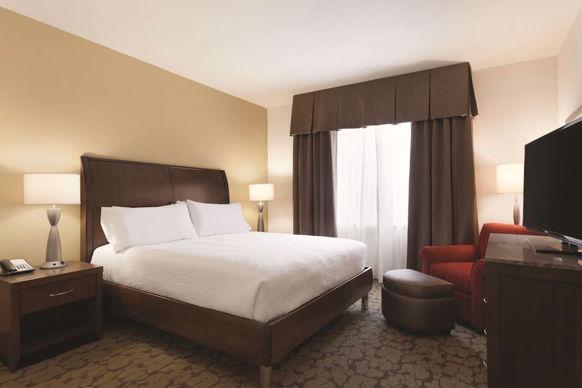 A hotel room with a large bed, a desk with a lamp, a television, and a red chair.
