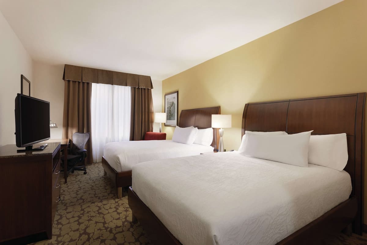 A hotel room with two beds, a desk with a TV, and a chair.
