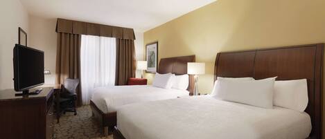 A hotel room with two beds, a desk with a TV, and a chair.