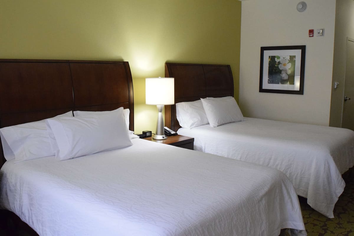 A hotel room with two beds, a nightstand with a lamp, a framed picture on the wall, and a door.