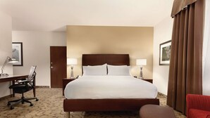 A hotel room with a large bed, a desk with a chair, a lamp, and a red armchair.