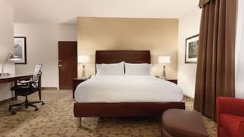 A hotel room with a large bed, a desk with a chair, a lamp, and a red armchair.