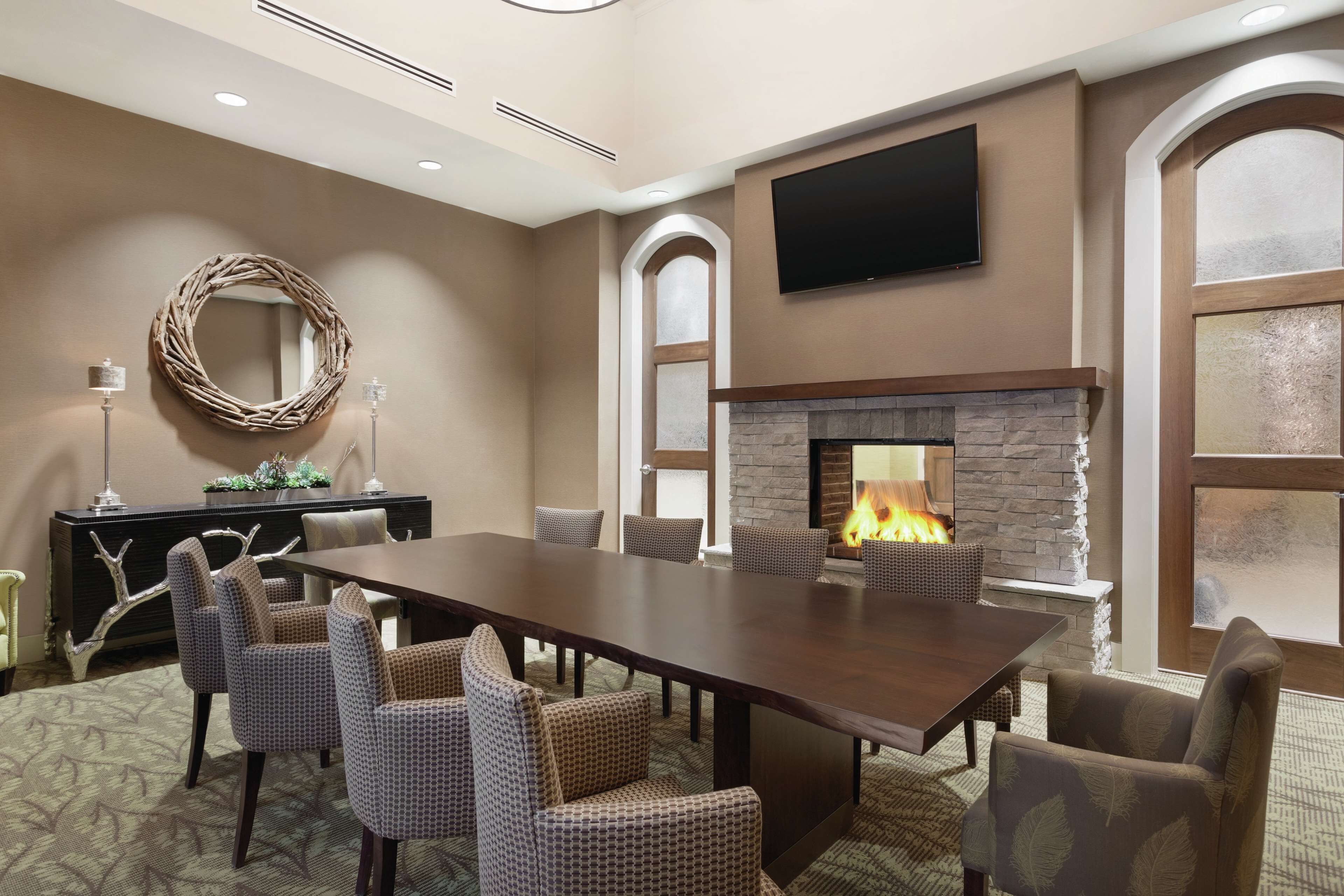 A meeting room with a long table, chairs, a fireplace, a television, and a decorative mirror.
