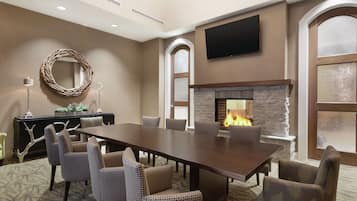 A meeting room with a long table, chairs, a fireplace, a television, and a decorative mirror.