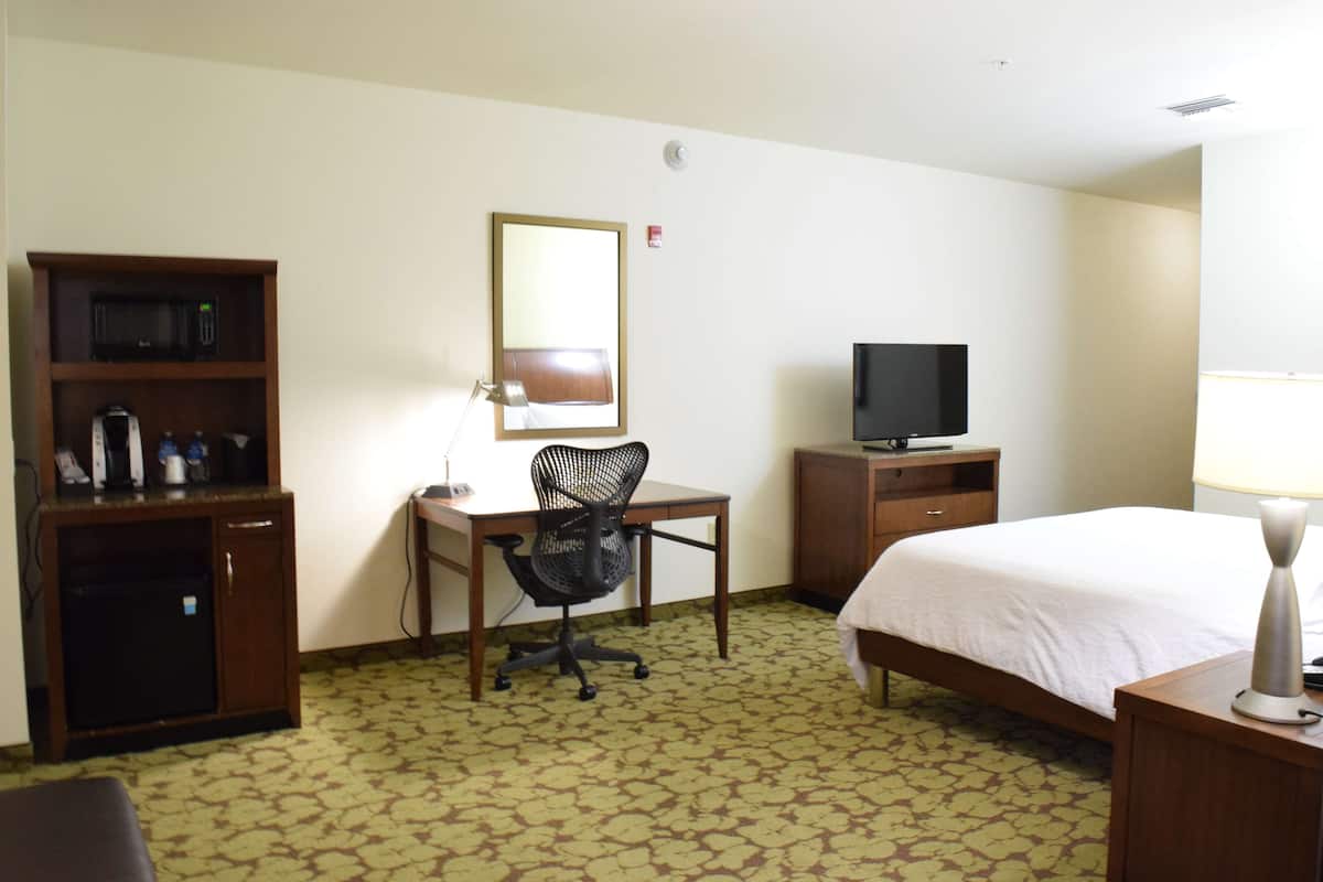 A hotel room with a bed, desk, chair, television, and a minibar.