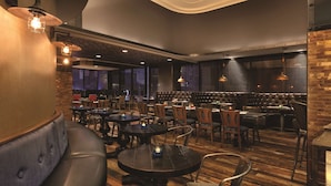 A restaurant interior with leather booths, round tables, and hanging pendant lights. - Hilton Garden Inn Rochester Downtown, NY (Rochester)