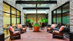A courtyard with wicker chairs, a central potted plant, and a stone wall. - Hilton Garden Inn Rochester Downtown, NY (Rochester)