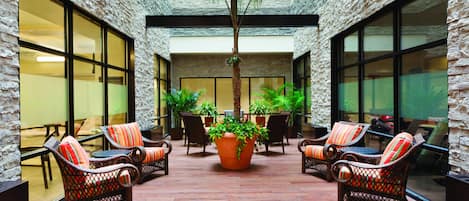 A courtyard with wicker chairs, a central potted plant, and a stone wall.