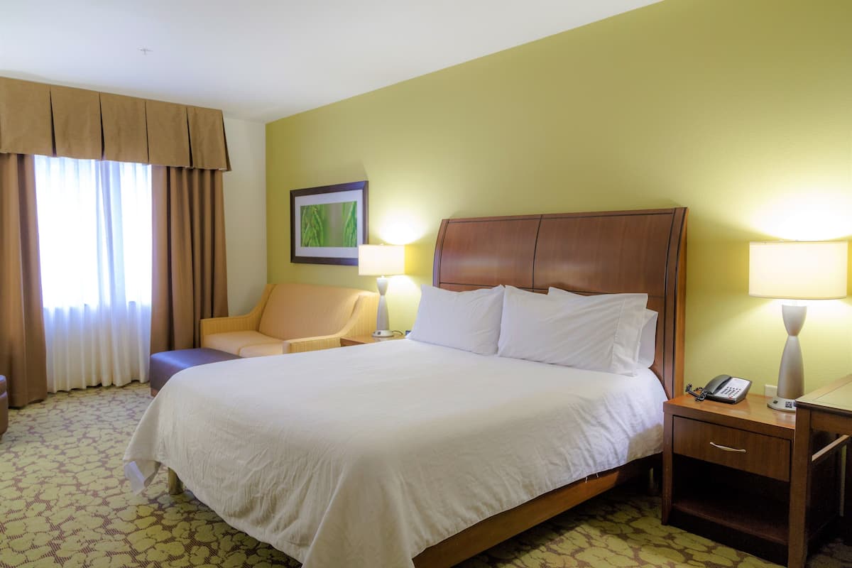 A hotel room with a large bed, a chair, a nightstand with a phone, and a lamp.