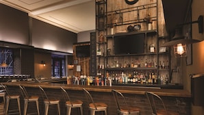 A bar area with stools, shelves of bottles, and a television mounted on the wall. - Hilton Garden Inn Rochester Downtown, NY (Rochester)