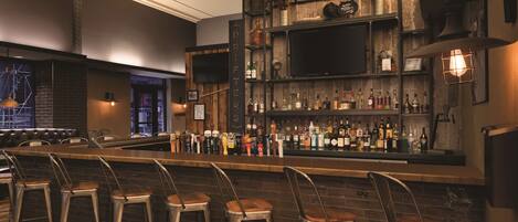 A bar area with stools, shelves of bottles, and a television mounted on the wall.