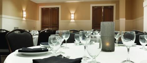 A dining area with round tables set for a meal, each with plates, cutlery, and wine glasses.