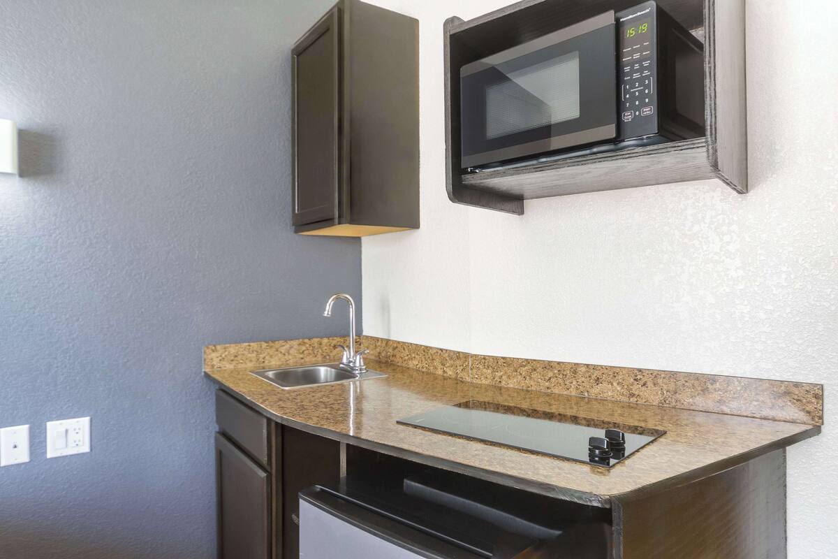 A compact kitchen with a granite countertop, stainless steel sink, and a microwave.
