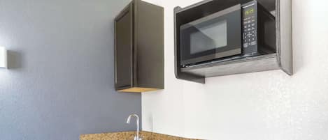 A compact kitchen with a granite countertop, stainless steel sink, and a microwave.
