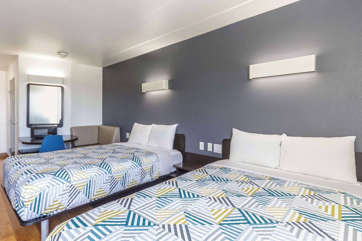 A hotel room with two beds, a desk, a chair, and a mirror.