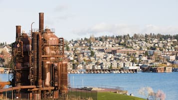 An industrial structure with multiple chimneys and pipes, a waterfront with boats, and a densely built residential area in the background.