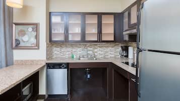 A modern kitchen with dark cabinets, a stainless steel refrigerator, a dishwasher, and a tiled backsplash.
