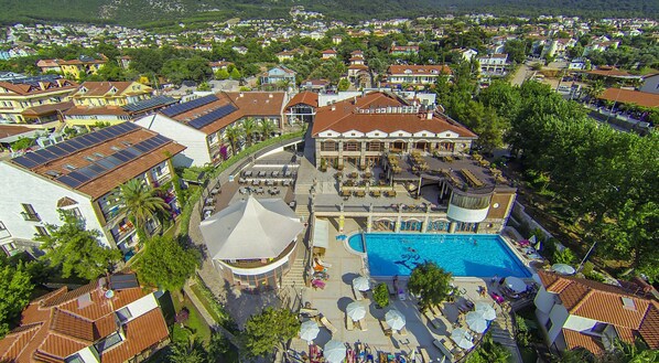 Relax by the resort's pool surrounded by sun loungers and umbrellas, amidst lush green surroundings.