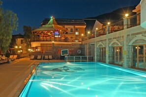 Relax by the pool with lounge chairs and umbrellas, overlooking the building's balcony with arched windows.