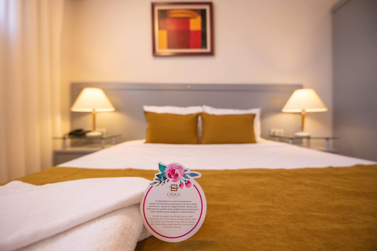 Une chambre d’hôtel avec un lit soigneusement fait, deux lampes de chevet et une carte décorative posée sur le lit.