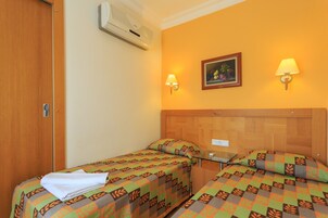A hotel room with two beds, a wooden headboard, an air conditioning unit, a framed picture on the wall, and two wall-mounted lamps.