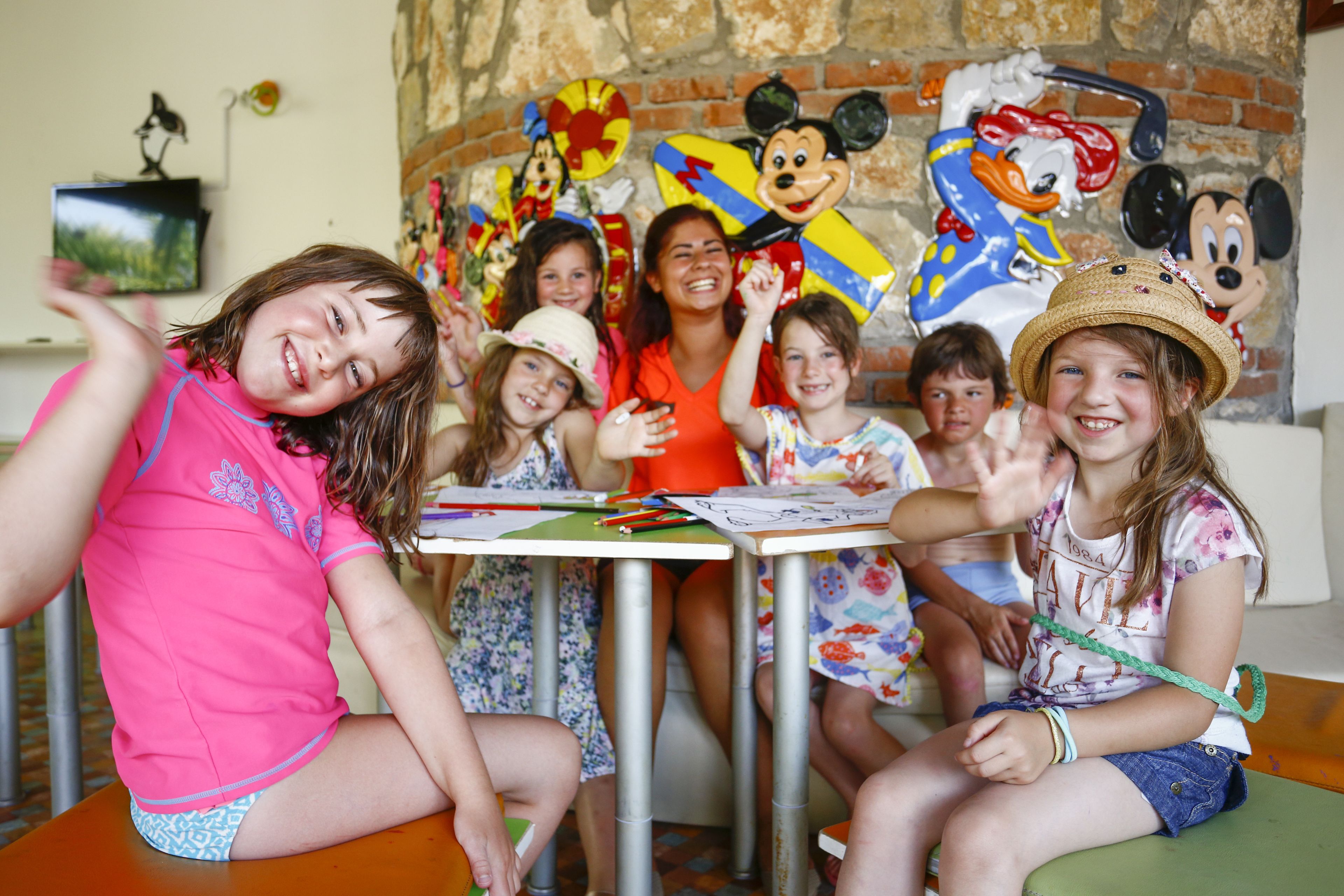A group of children seated at a table with Mickey Mouse decorations in the background.