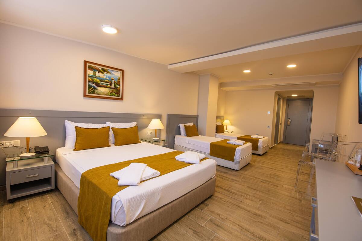Une chambre d’hôtel avec deux lits, un bureau et une chaise. Il y a un tableau au mur et une porte à l’arrière-plan.