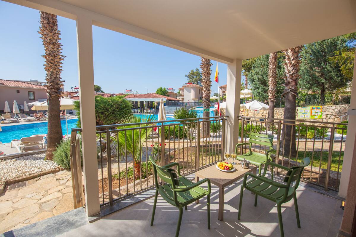 Un balcon avec une table et des chaises donnant sur une piscine et un bâtiment dont les toits sont recouverts de tuiles rouges.