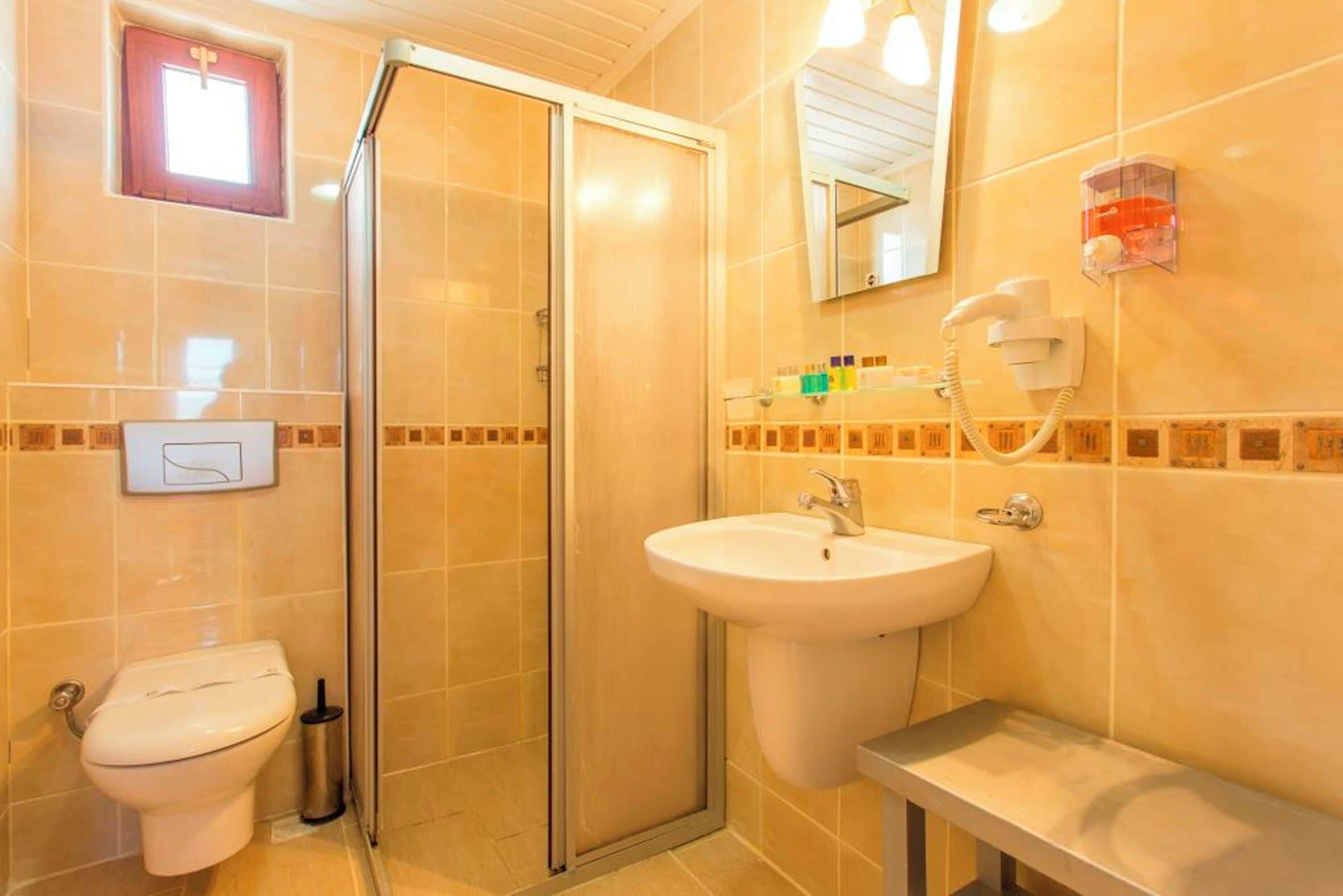 A bathroom with a toilet, a sink, a shower with a glass door, a mirror, and a hairdryer on the wall.