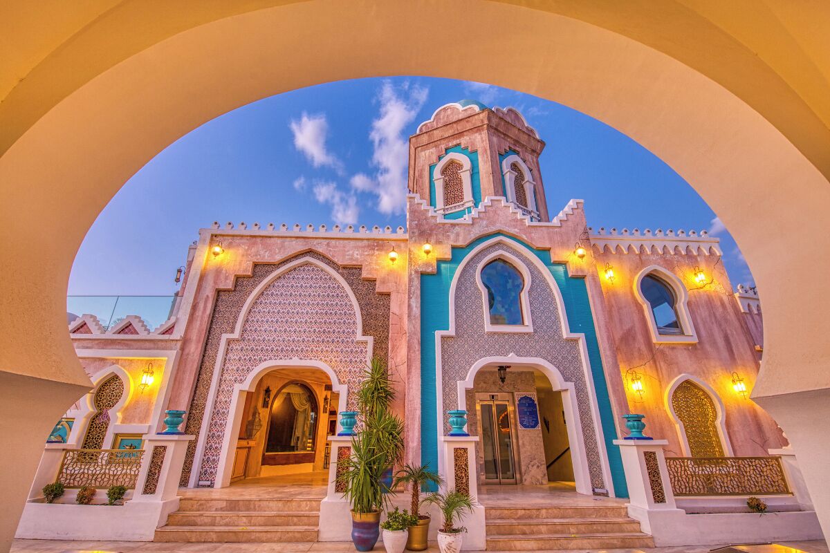 A traditional building with arched doorways and a tower, featuring decorative lighting and potted plants.