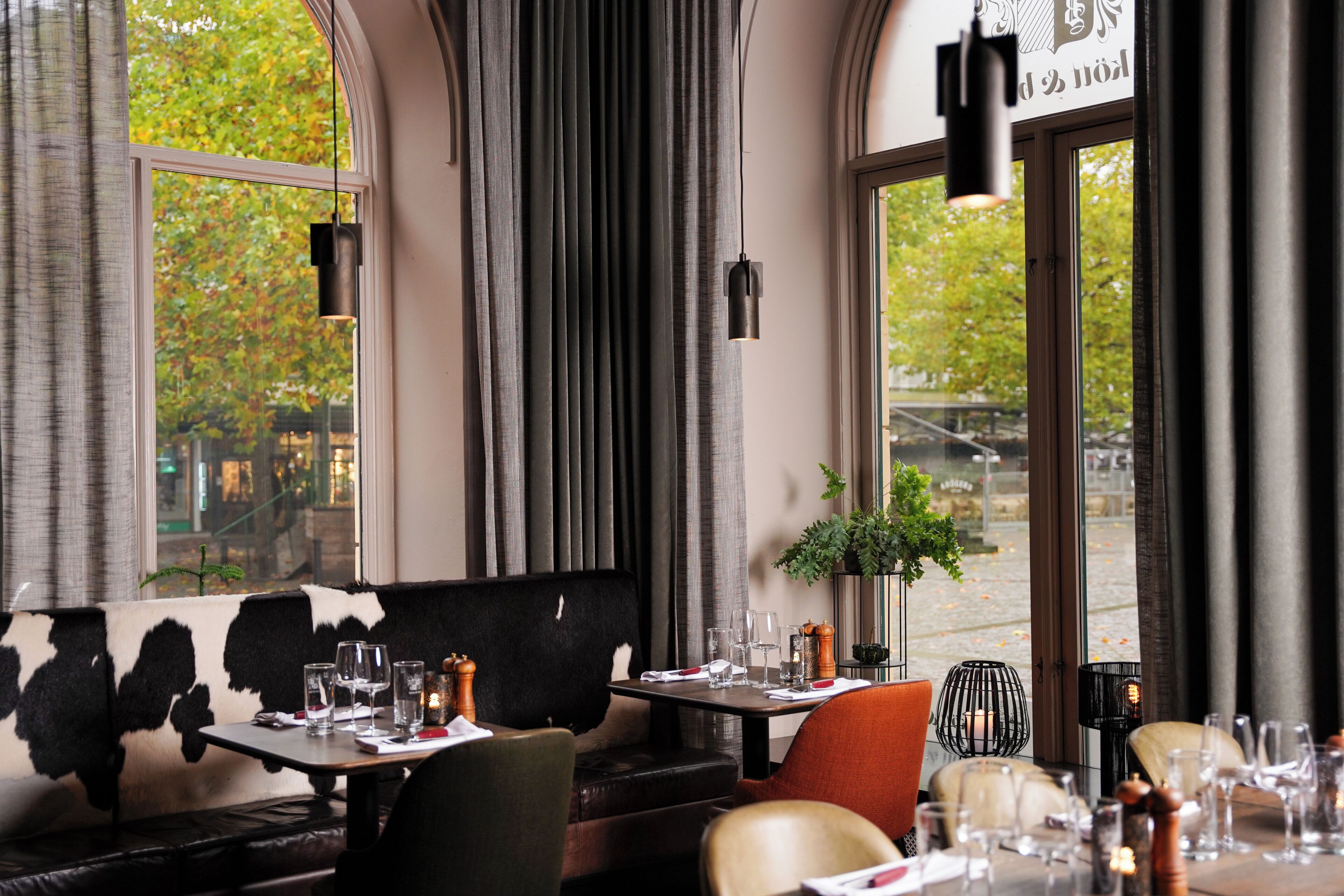 Interior de un restaurante con una mesa alta, sillas y vistas al exterior.