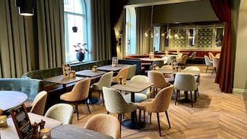 A restaurant with wooden tables and chairs, large windows, and a herringbone floor pattern.