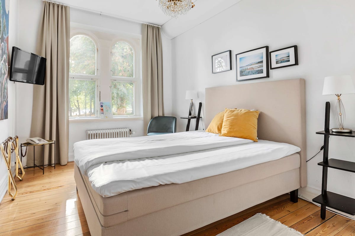 Ein Hotelzimmer mit Bett, Sessel, Schreibtisch, Lampe und Fernseher.