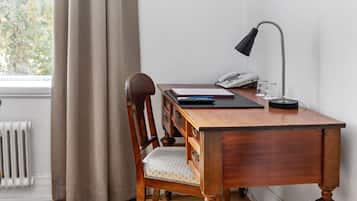 Een houten bureau met een stoel, een lamp, een telefoon en een raam met gordijnen.