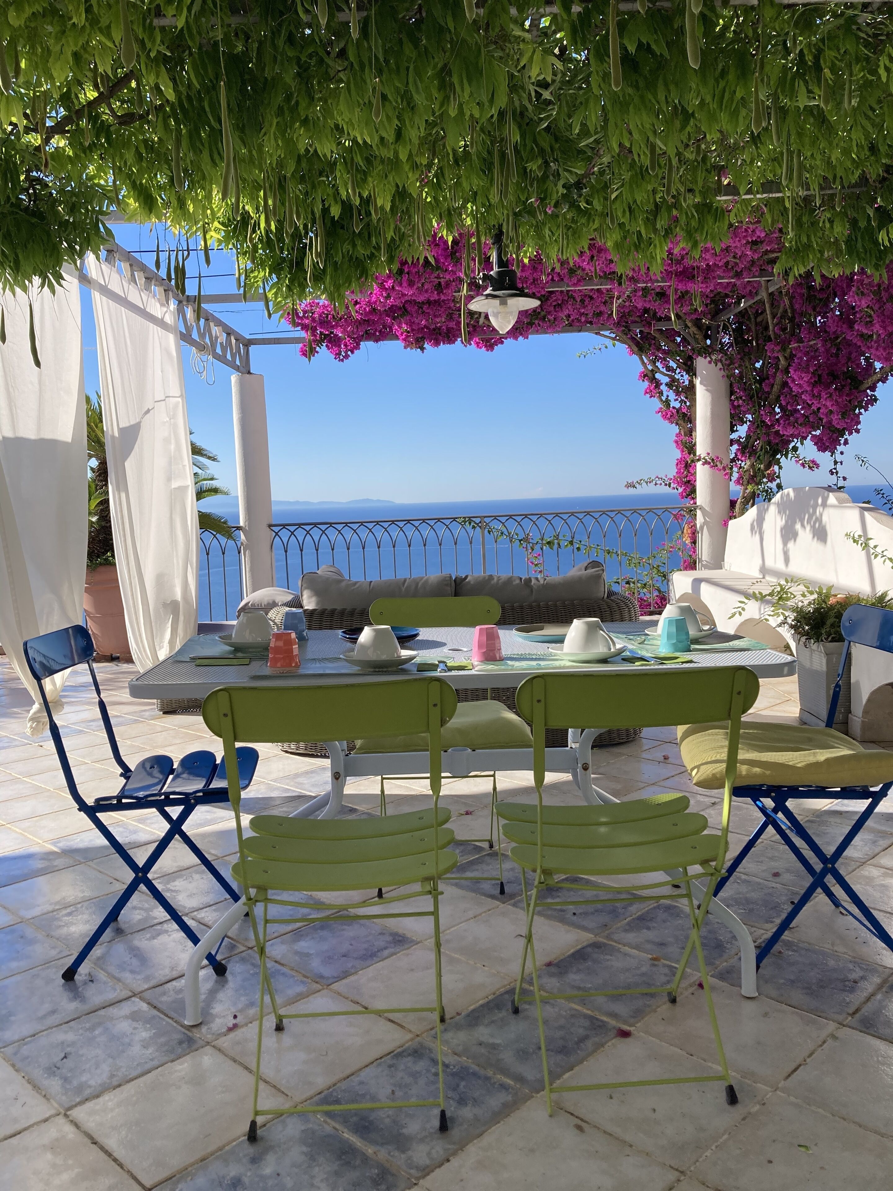 Un patio al aire libre con una mesa lista para comer, sillas y vistas al mar.