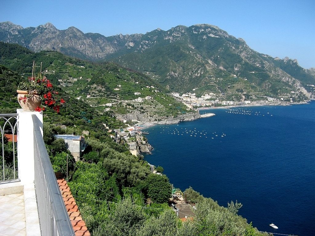 A coastal town with terraced houses, a clear blue sea, and mountains in the background.