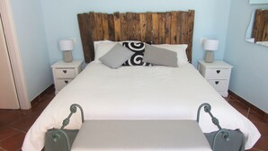Una cama bien hecha con un cabecero de madera, dos mesitas de noche con lámparas y un banco al pie de la cama.