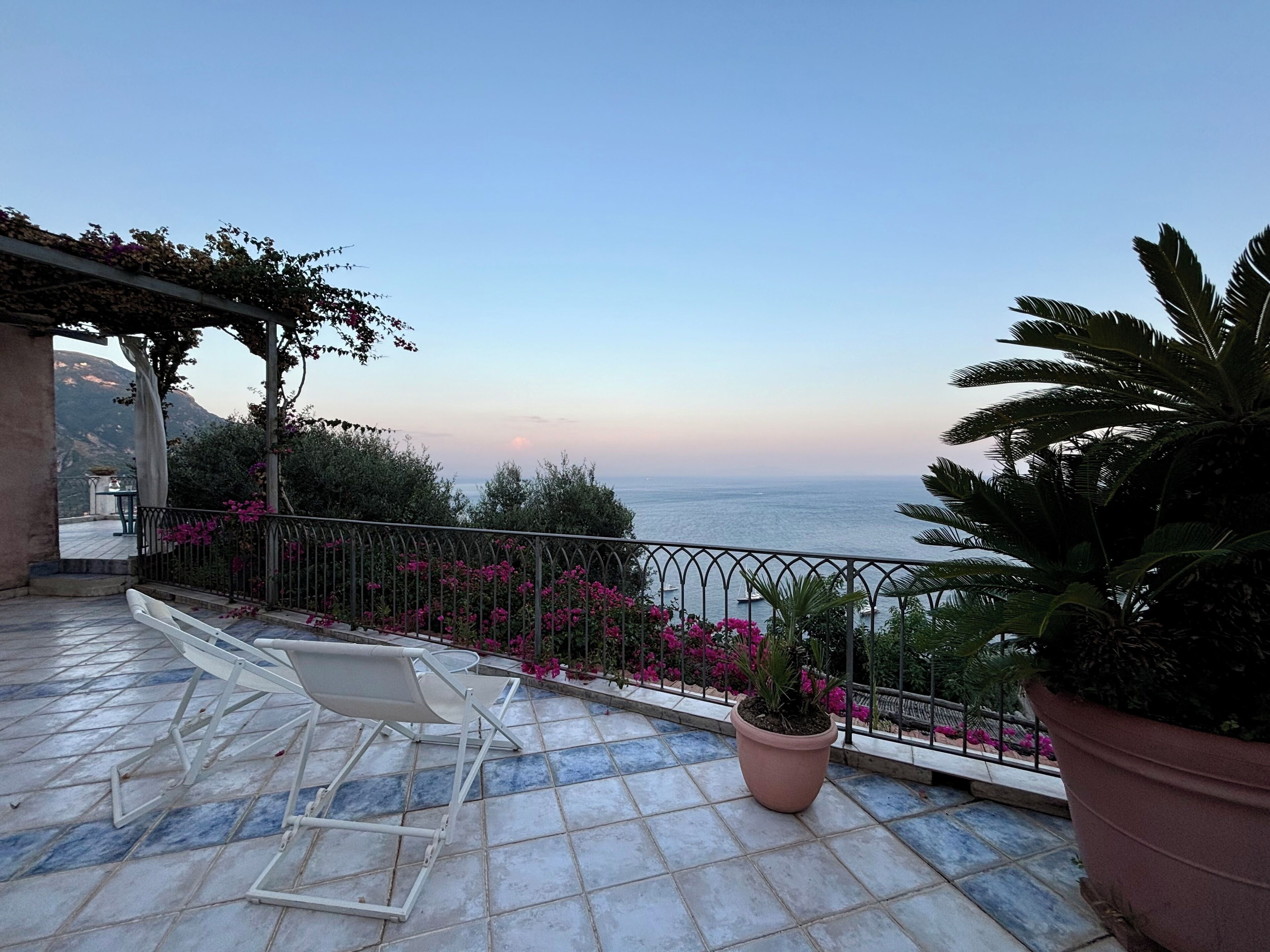Un balcon avec vue sur la mer, une chaise blanche et des plantes en pot.