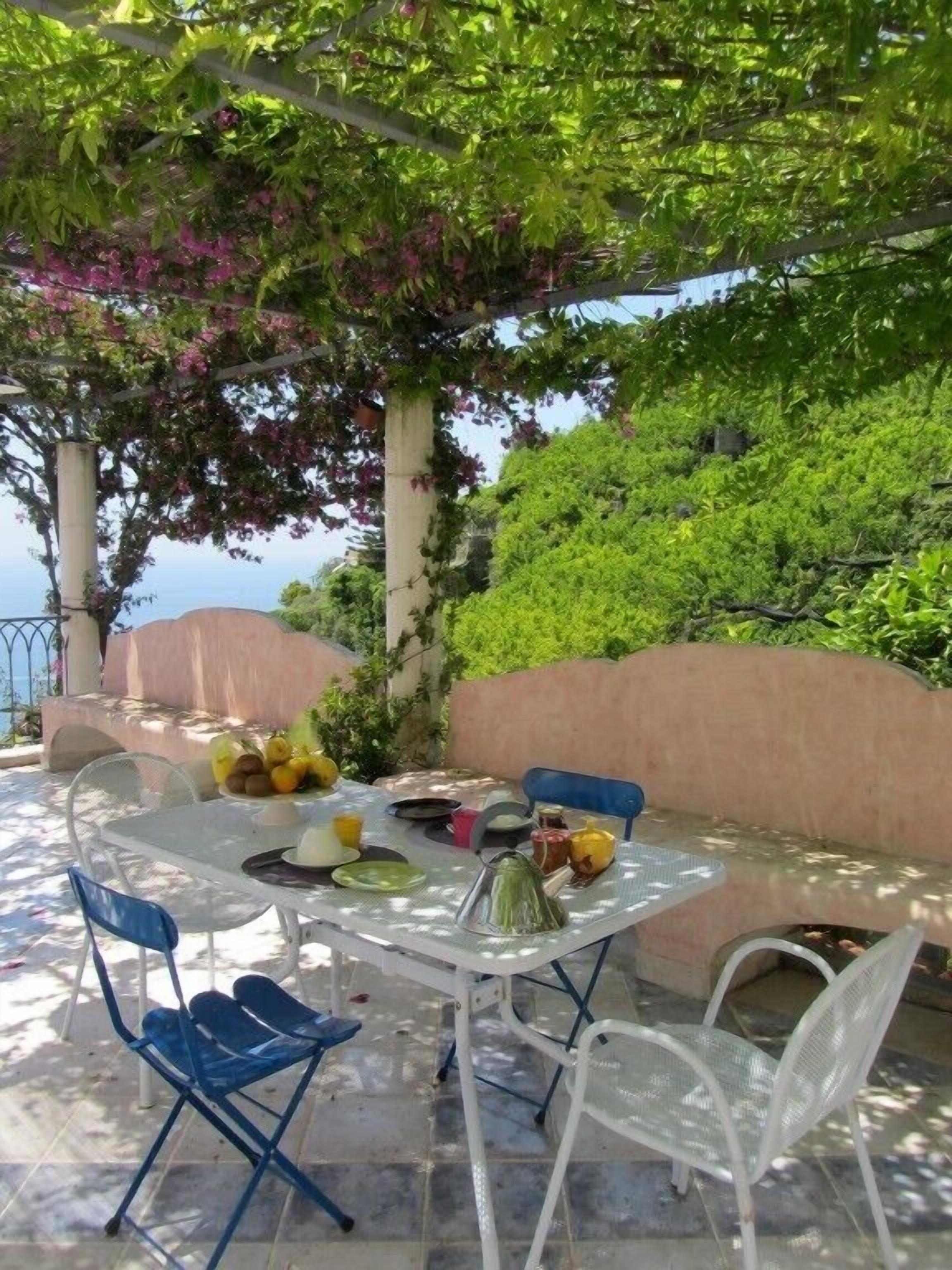 Un área de comedor al aire libre con una mesa y sillas, rodeada de vegetación y vista al mar.
