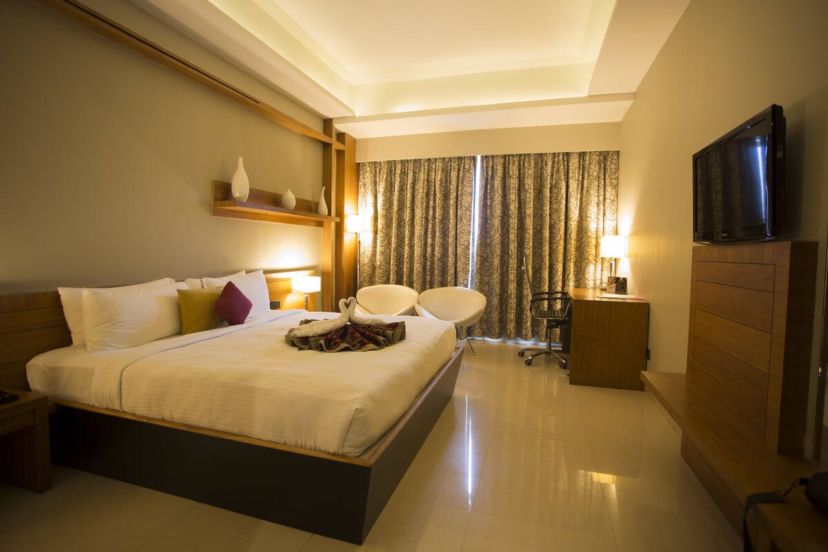 A hotel room with a large bed, bedside tables, a flat-screen TV, a desk with a lamp, and a chair.