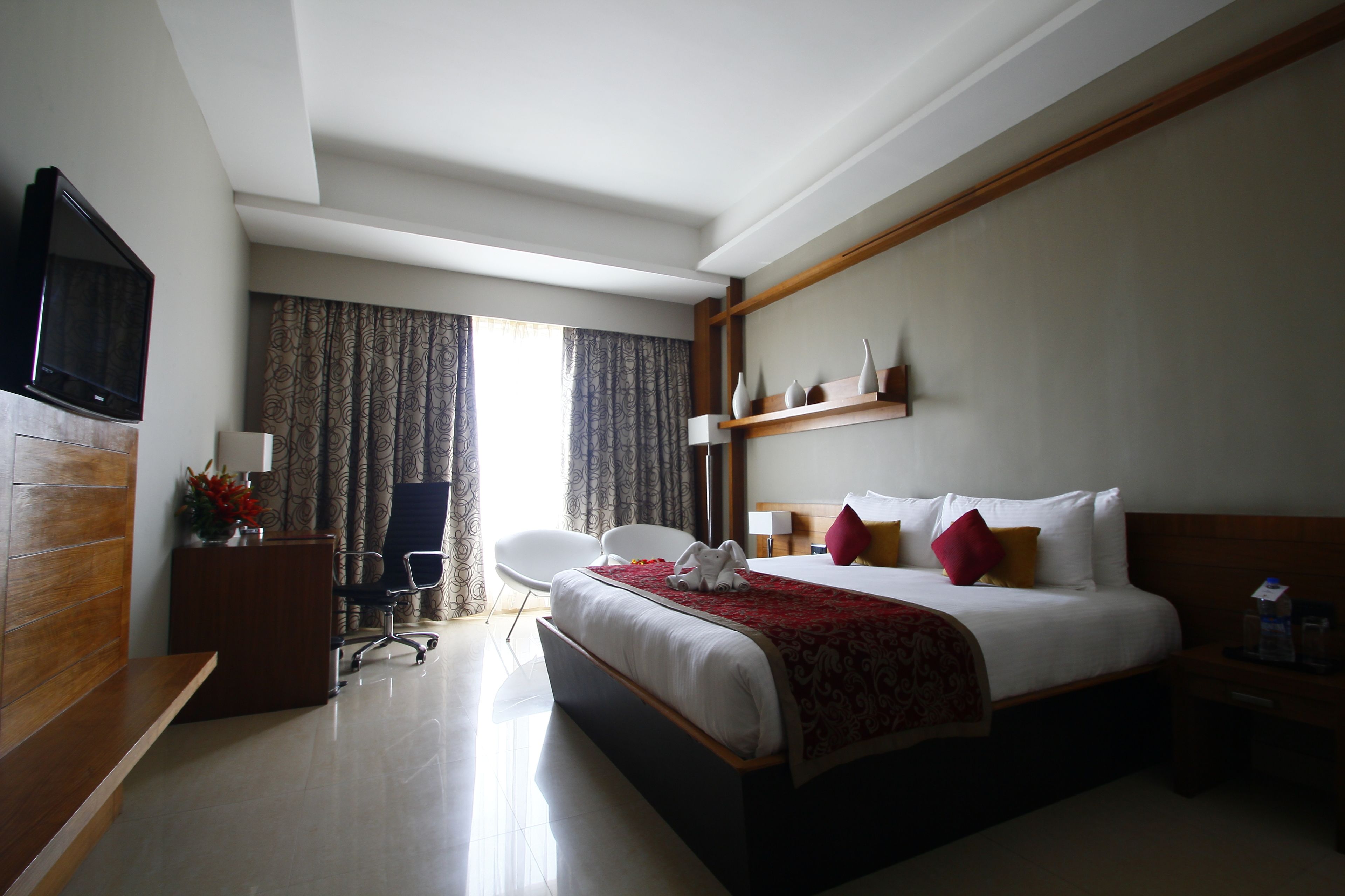 Habitación de hotel con cama, escritorio, silla, televisión y ventana con cortinas.