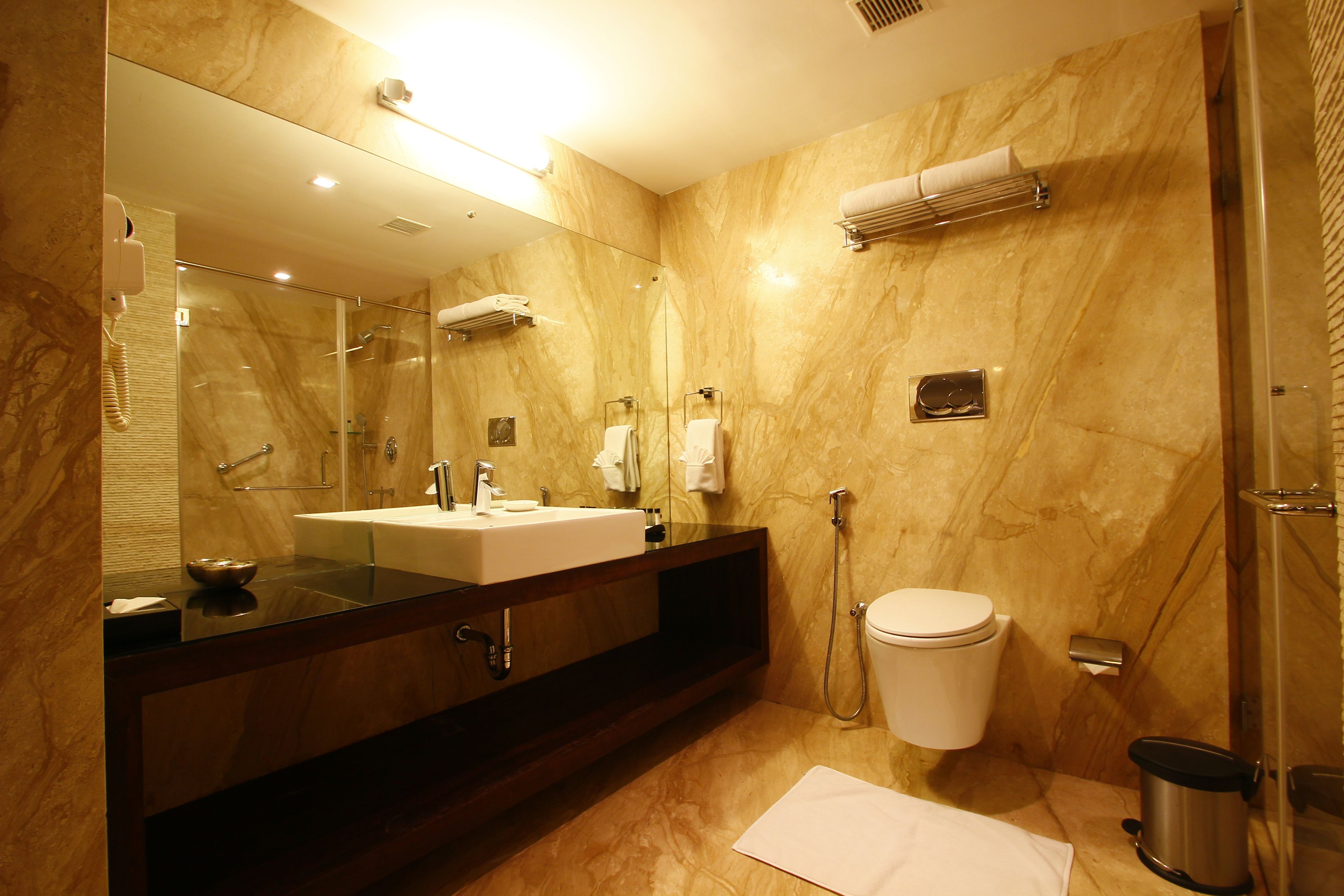 Een moderne badkamer met een marmeren wand, een grote spiegel, een wastafel, een toilet en een douchehoek.
