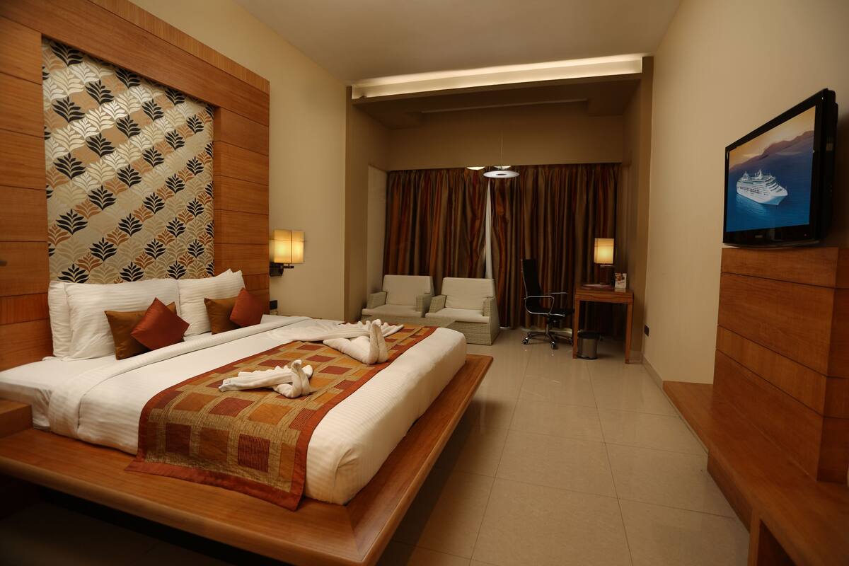 A hotel room with a large bed, a sofa, a desk, and a television displaying a cruise ship.