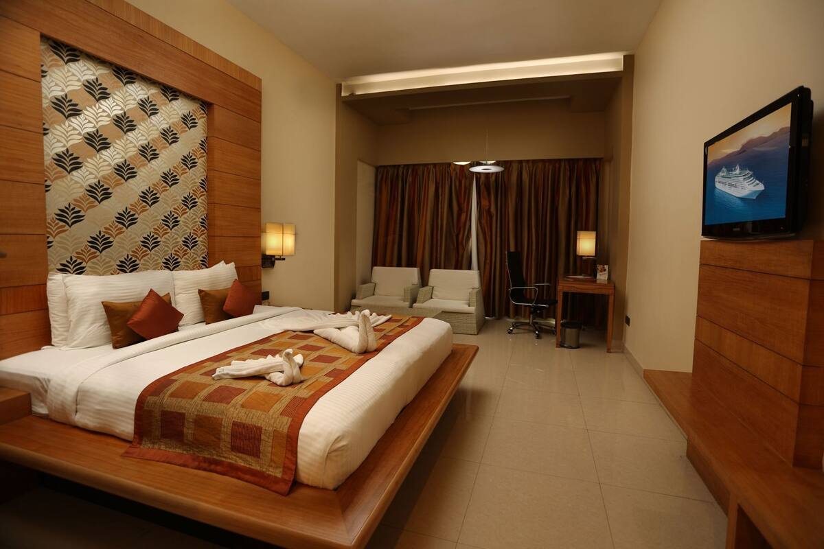 A hotel room with a large bed, a desk, a chair, a TV, and a view of the sea.