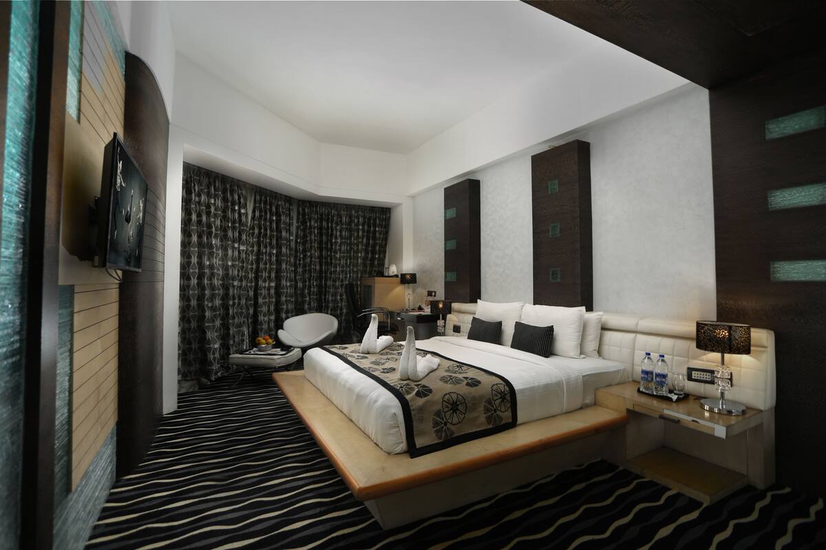 A modern hotel room with a large bed, a desk, a chair, a TV, and a bathroom.
