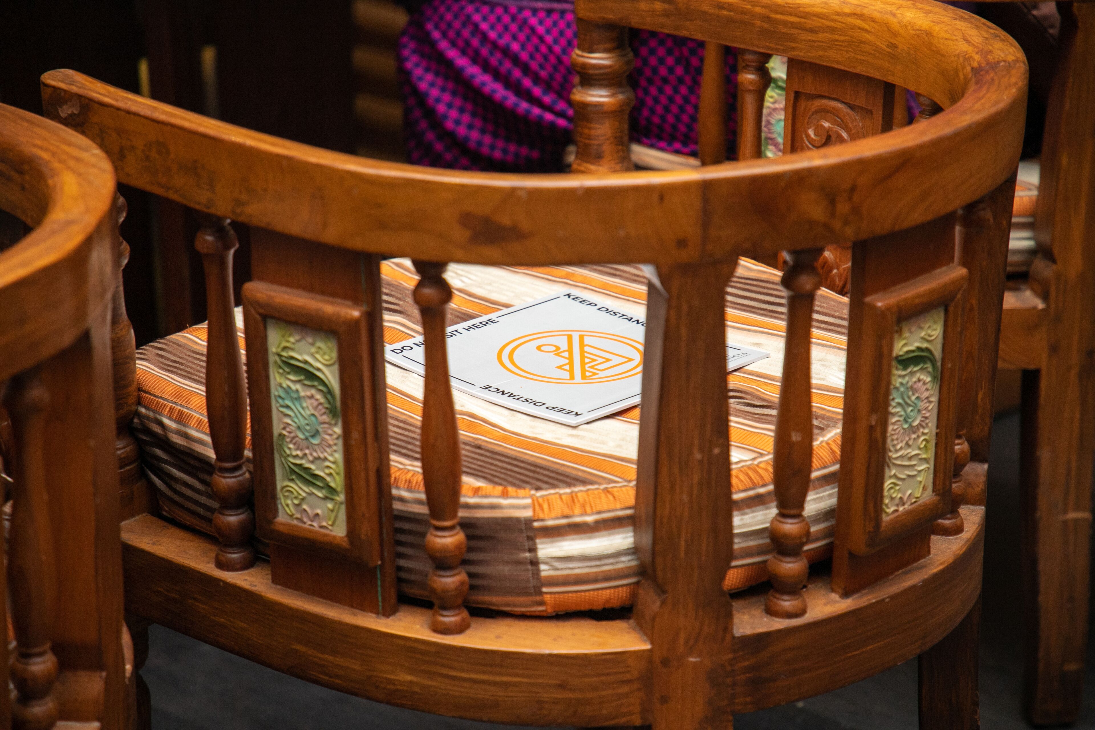 Una silla de madera con cojín que presenta un diseño geométrico y un letrero que dice 'KEEP DISTANCE'.