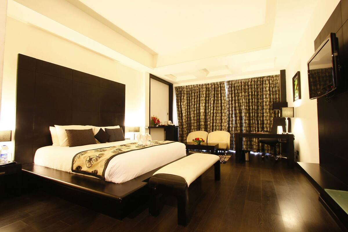 A hotel room with a large bed, a desk, a chair, a TV, and a curtain.