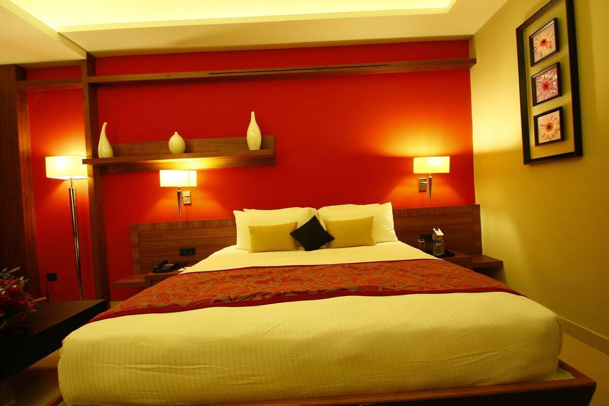 A hotel room with a large bed, two bedside lamps, a nightstand, and a red accent wall.