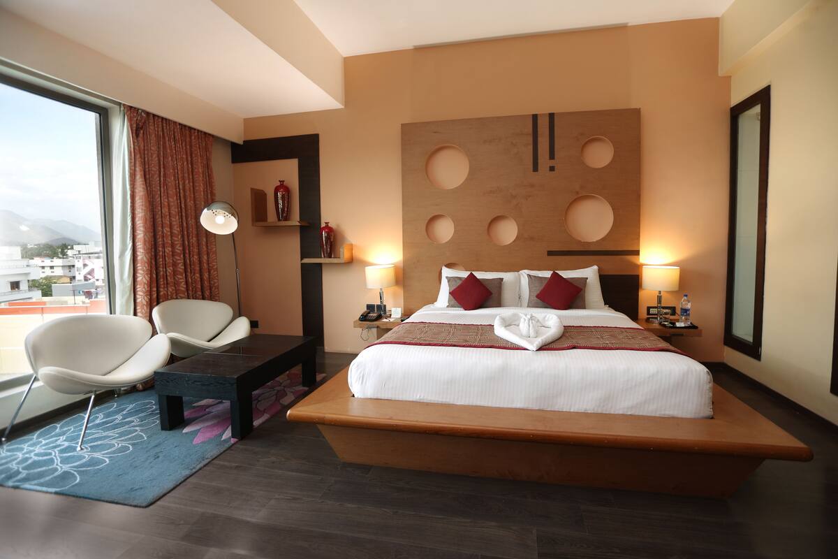 A hotel room with a large bed, two bedside tables, a desk, a chair, a large window, and a view of the city.